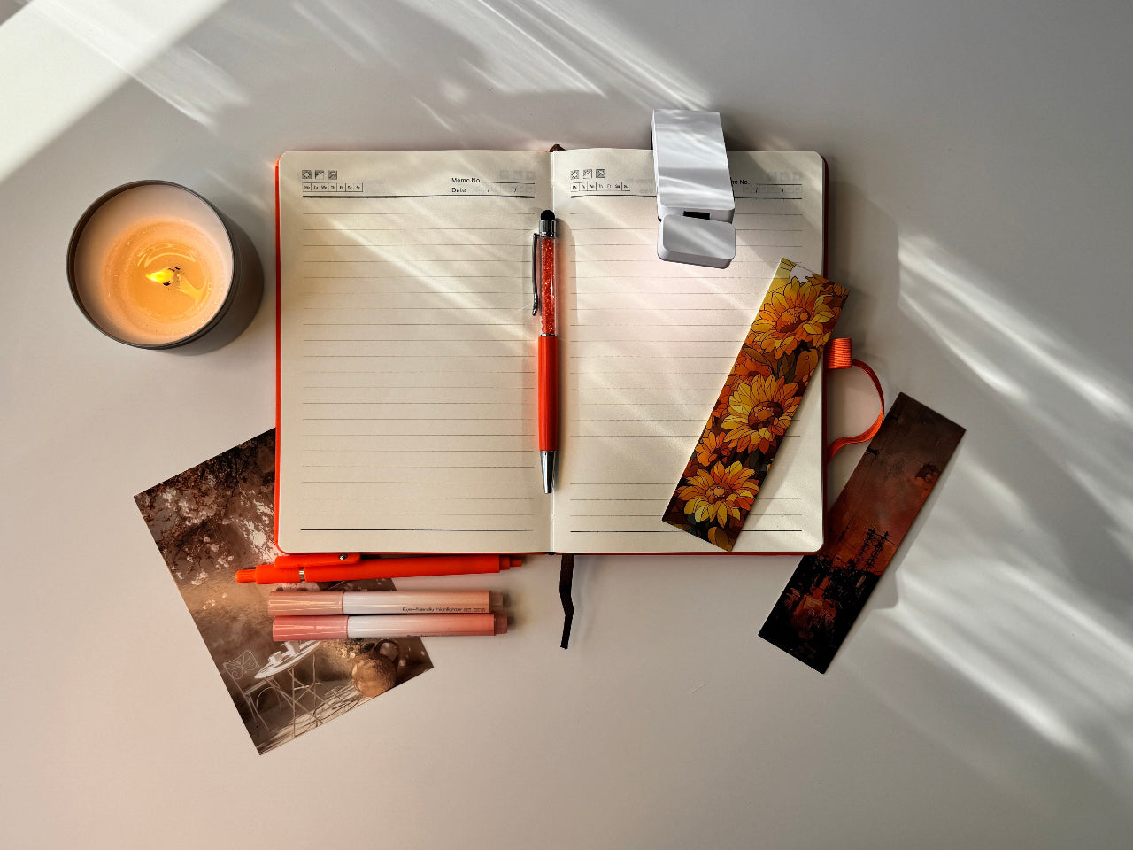 Open notebook with a pen, photos, and a lit candle on a white surface