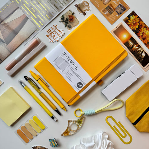 Yellow notebook surrounded by stationery items on a light surface
