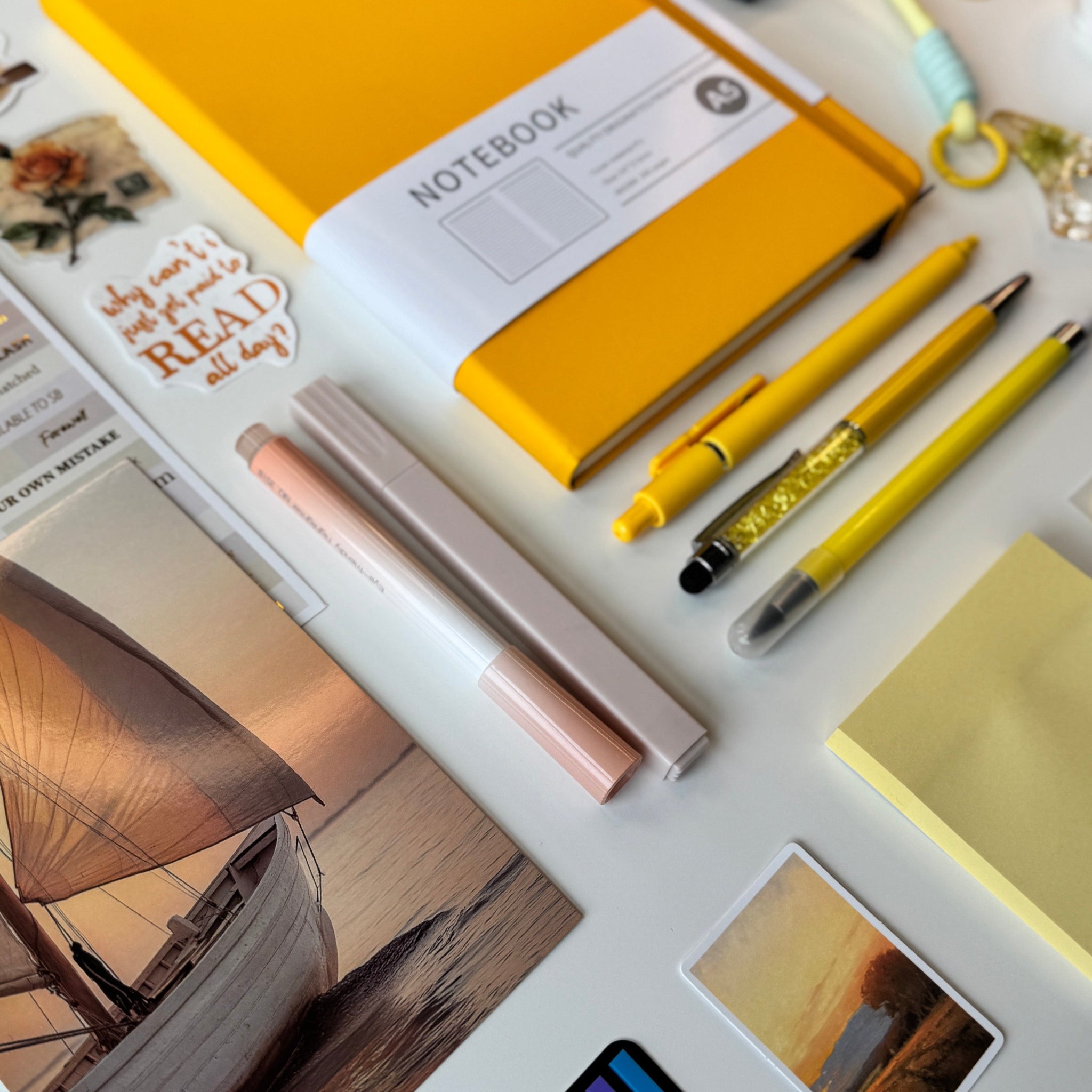 Yellow notebook, pens, and sticky notes on a white surface with scenic photos.