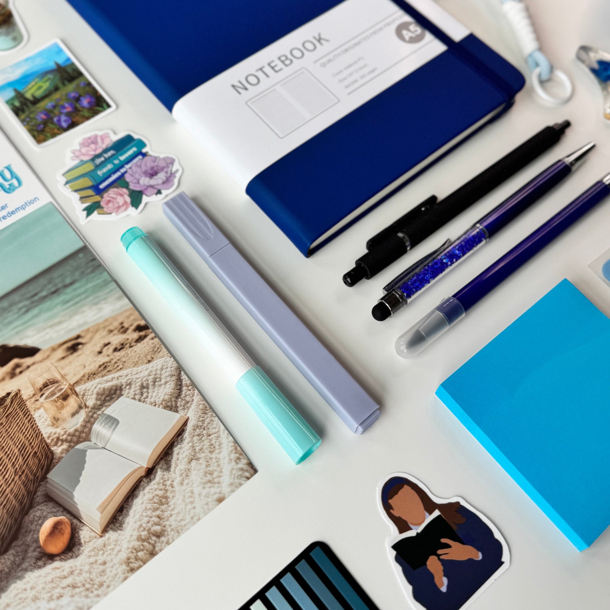 Collection of stationery items including a blue notebook, pens, and photo albums on a white surface.