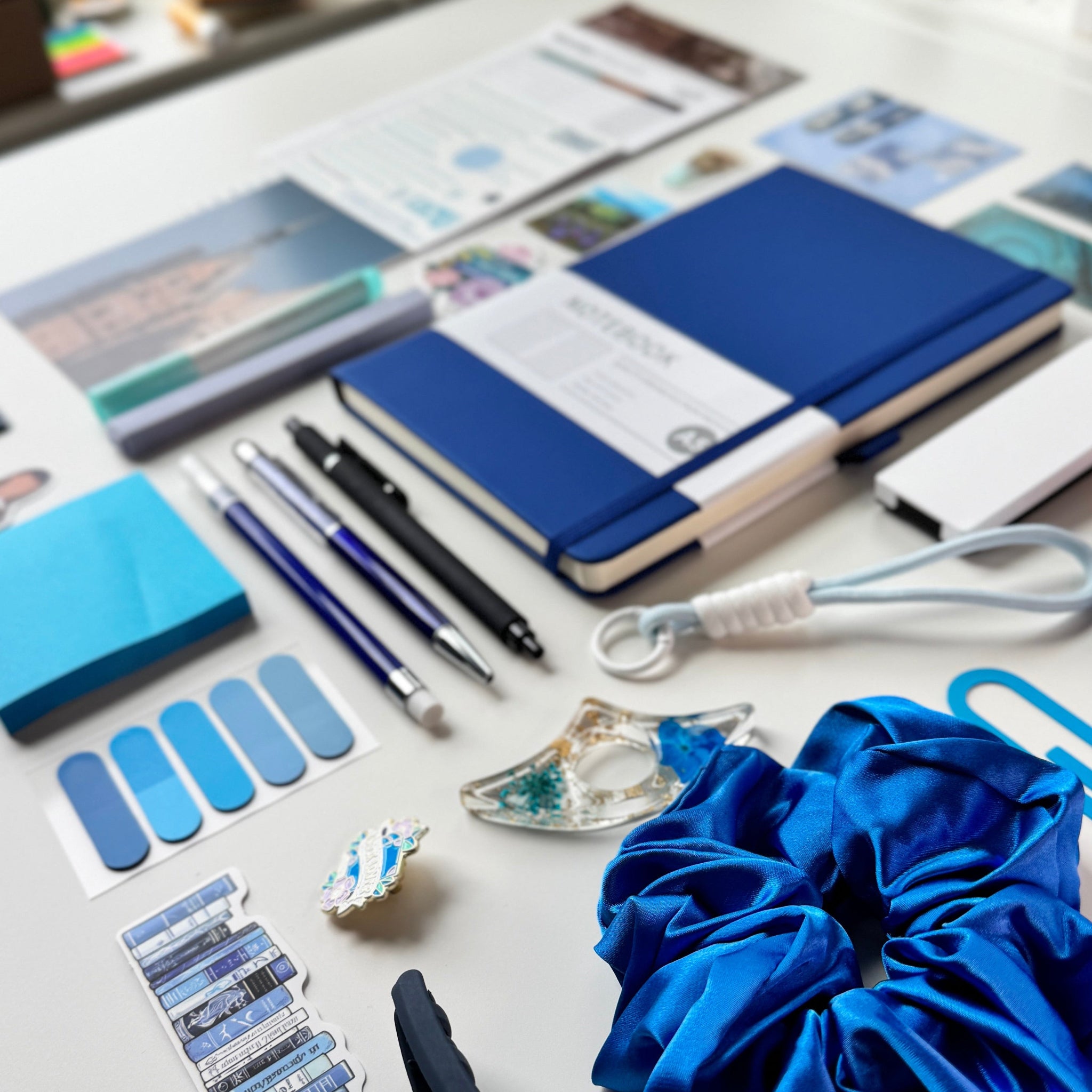 Desk with stationery items including notebooks, pens, and a blue scrunchie.