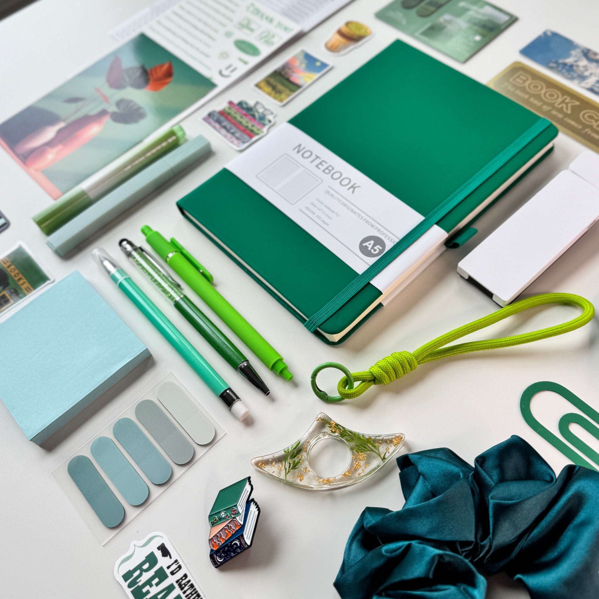 Collection of stationery items including a green notebook, pens, and other office supplies on a white surface.
