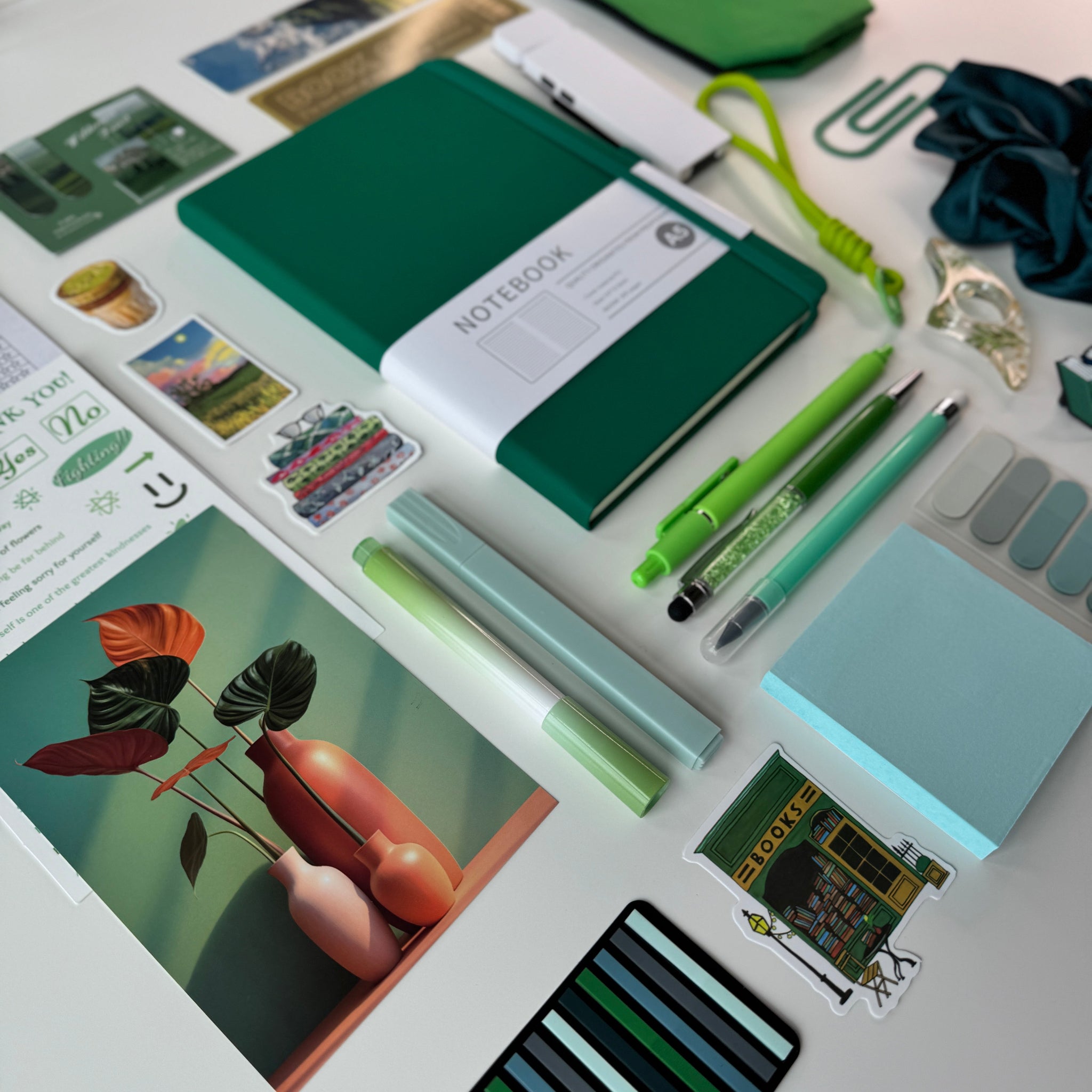 Collection of stationery items including a green notebook, pens, and cards on a white surface.