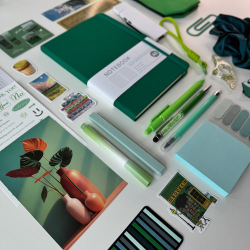 Collection of stationery items including a green notebook, pens, and cards on a white surface.